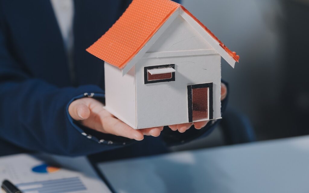 Realtor in Chandler AZ holding a house model to represent buying and selling real estate services.