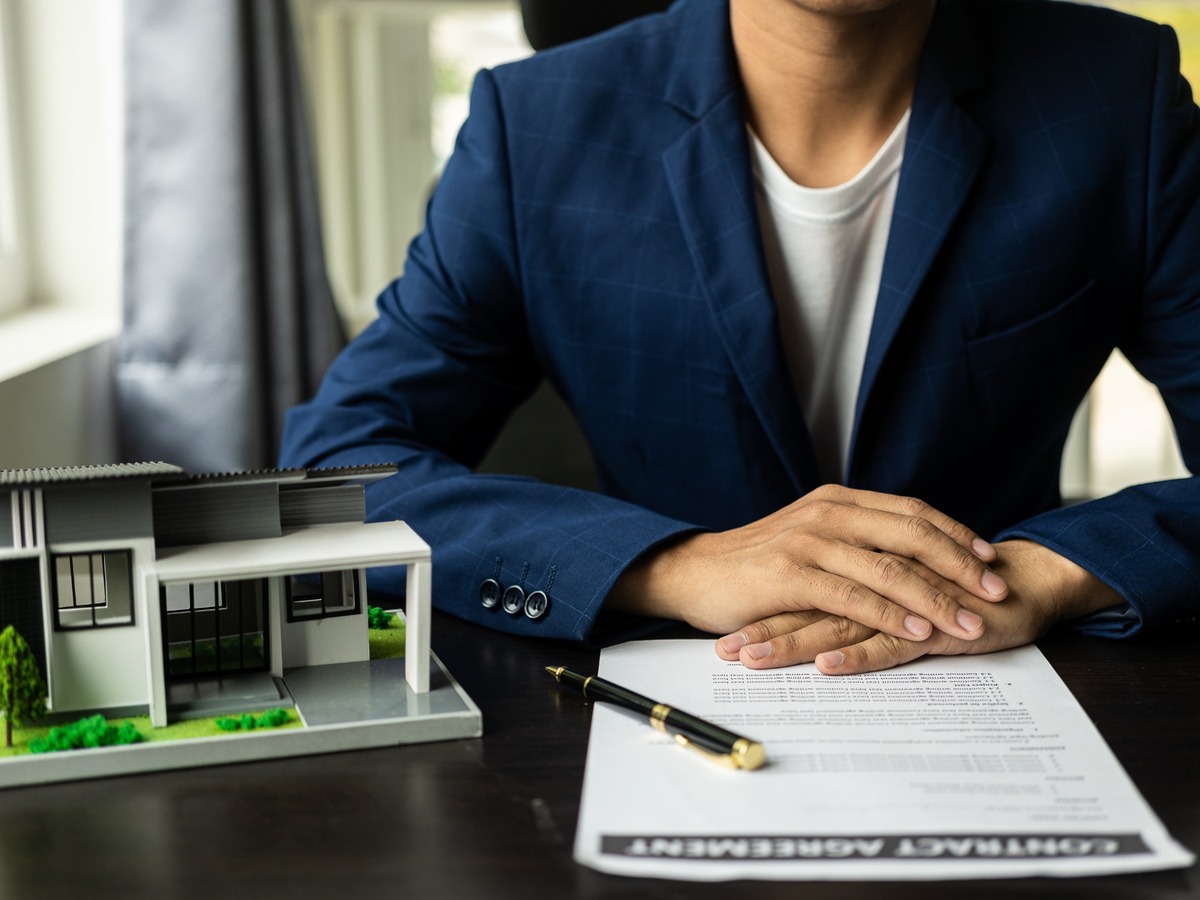 Real estate broker handing contract next to a model house real estate services