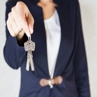 A real estate agent holding out a set of house keys, representing real estate ownership or a completed home purchase.