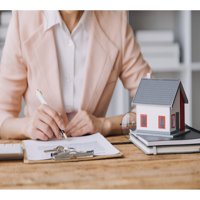 Business woman reviewing home valuation documents beside a small model house and keys on a desk.